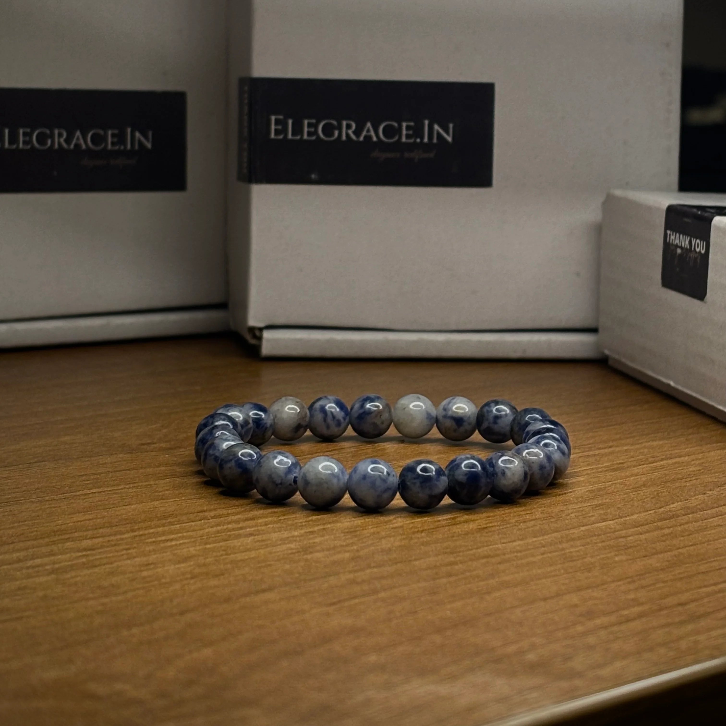 Blue beaded bracelet on a wooden surface with 'ELEGRACE.IN' branding in the background.